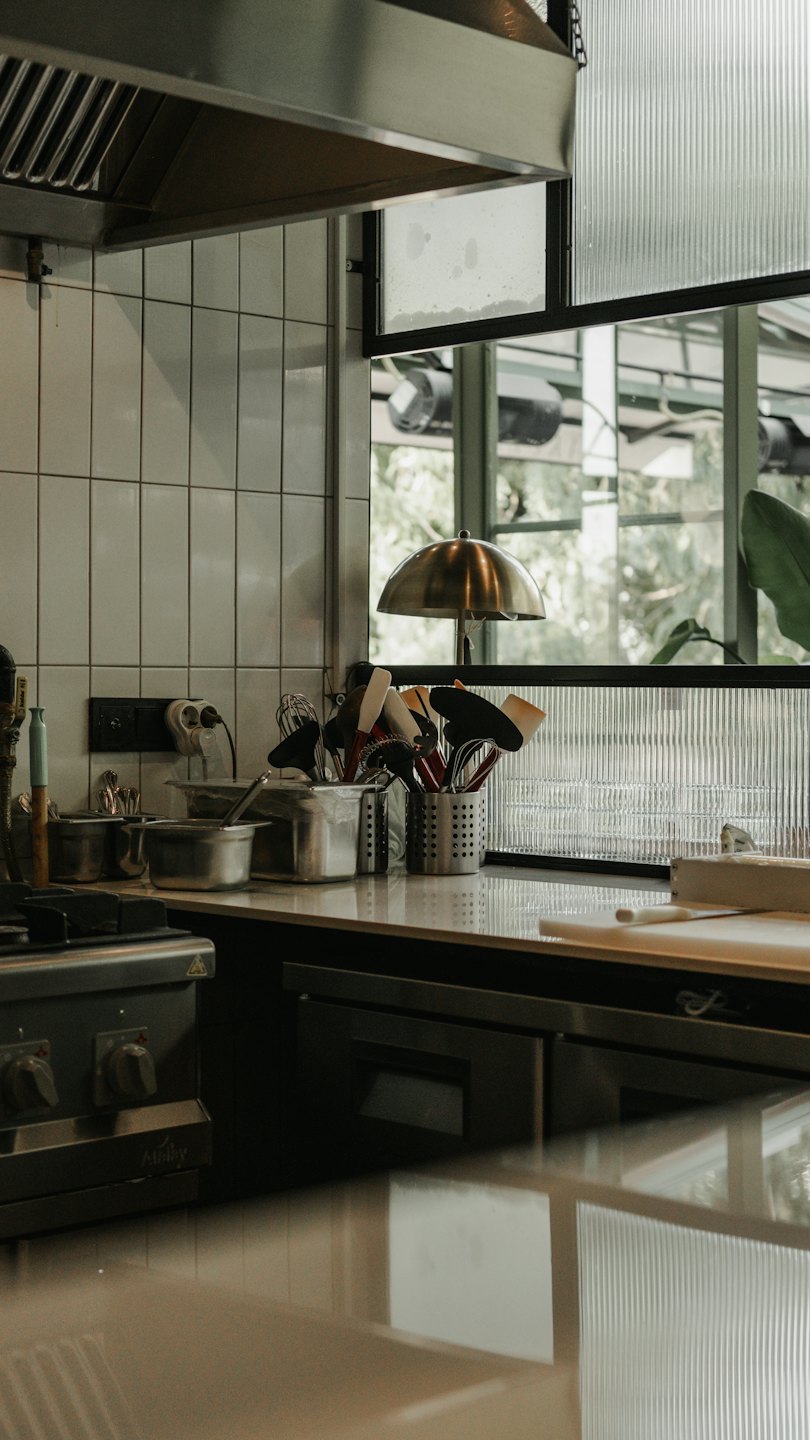 Professional kitchen counter with utensils and brass lamp.