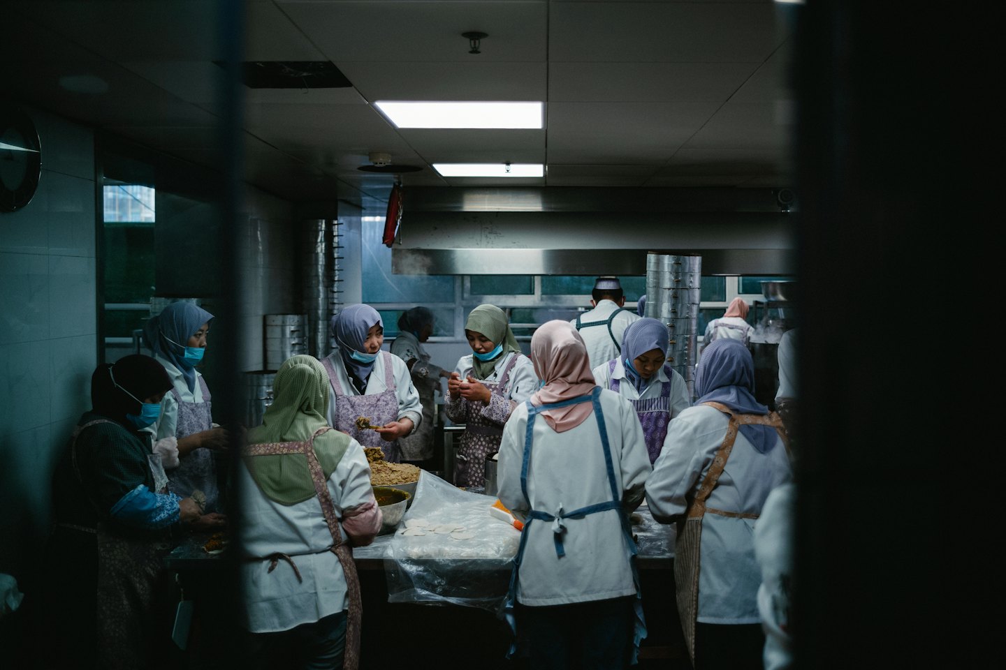 Women in uniforms prepare food on stainless steel kitchen tables.