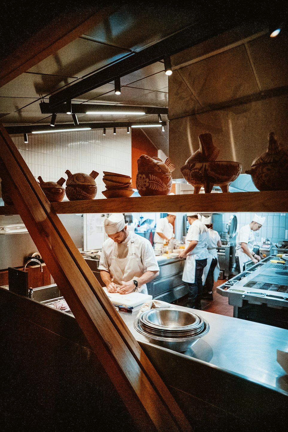 Chefs in uniforms prepare food inside a busy commercial kitchen.