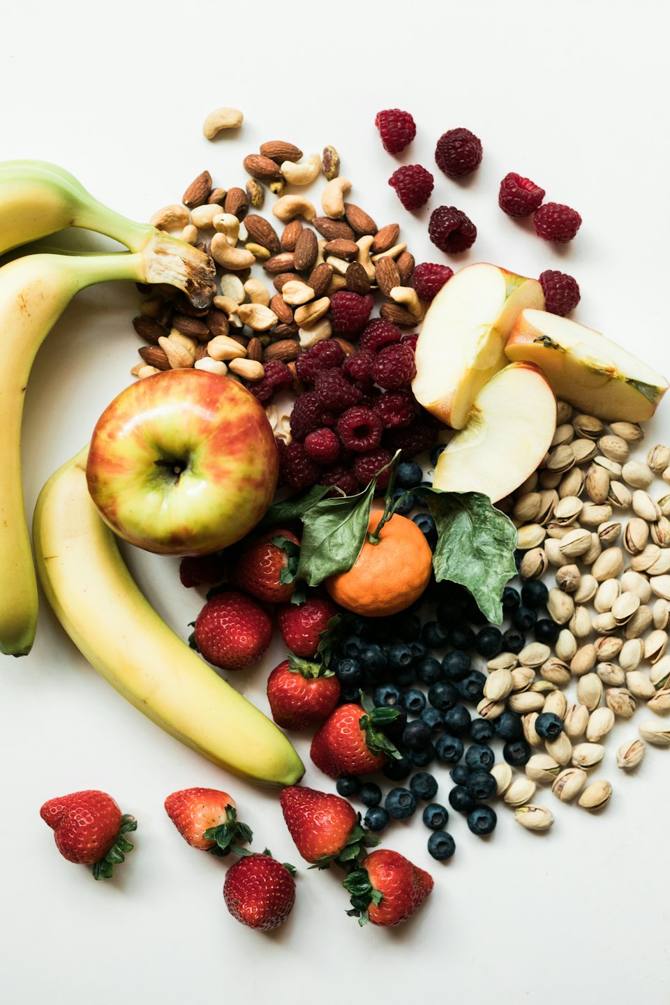 Assorted fresh fruits and nuts arranged on a white surface.
